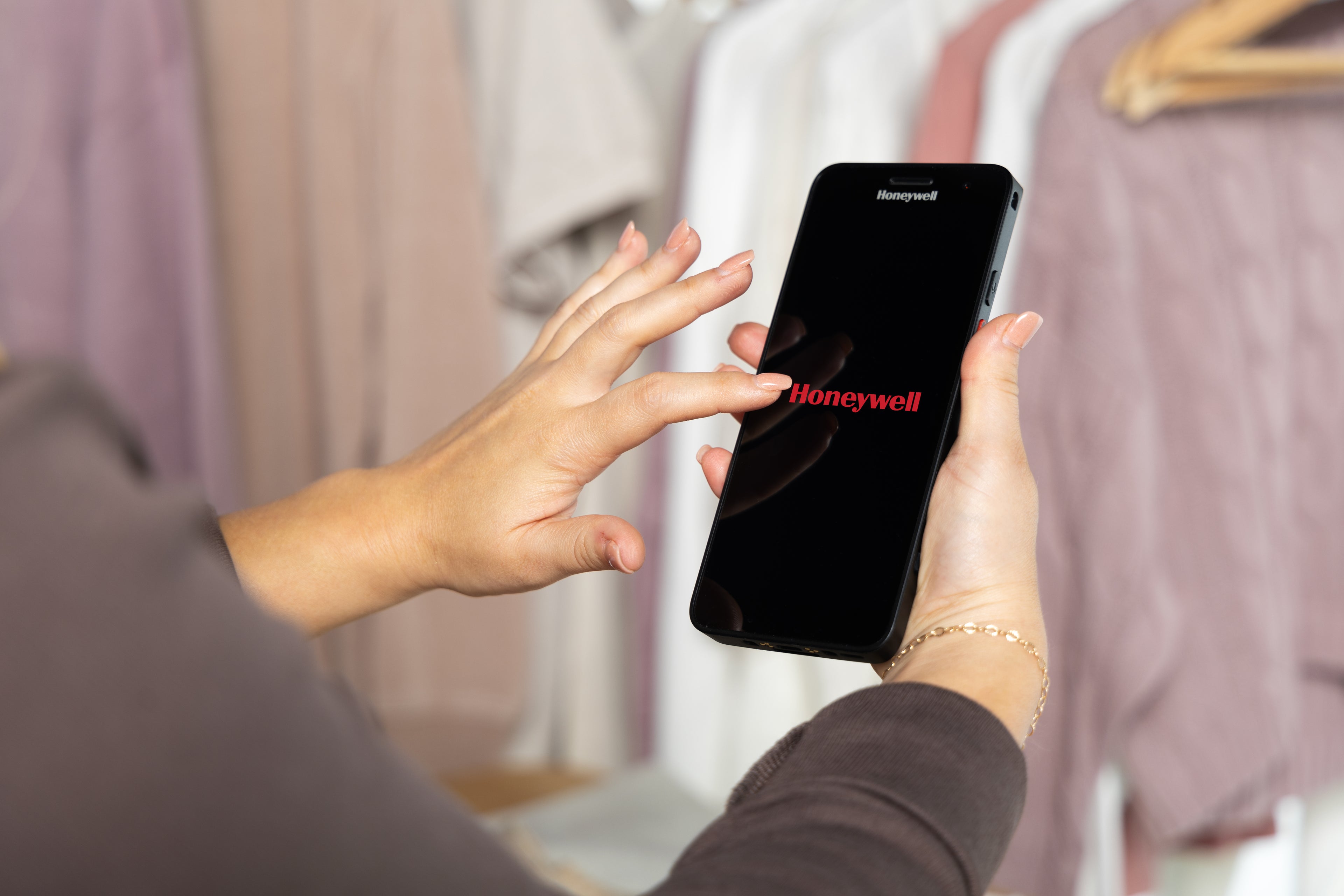Person holding a smartphone with Honeywell logo in front of clothing racks