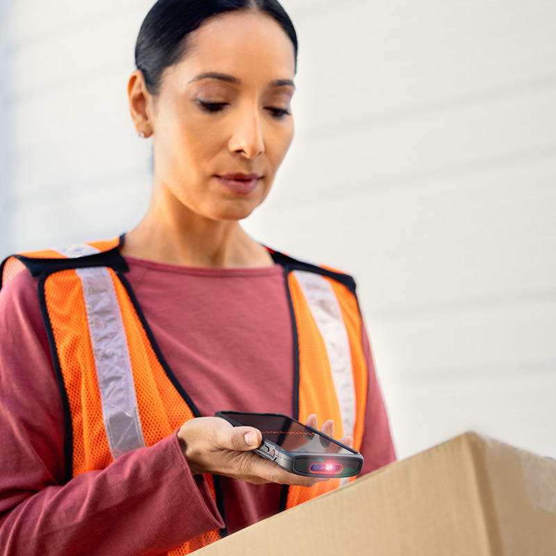 Person in orange safety vest using a handheld device with a box on a plain background