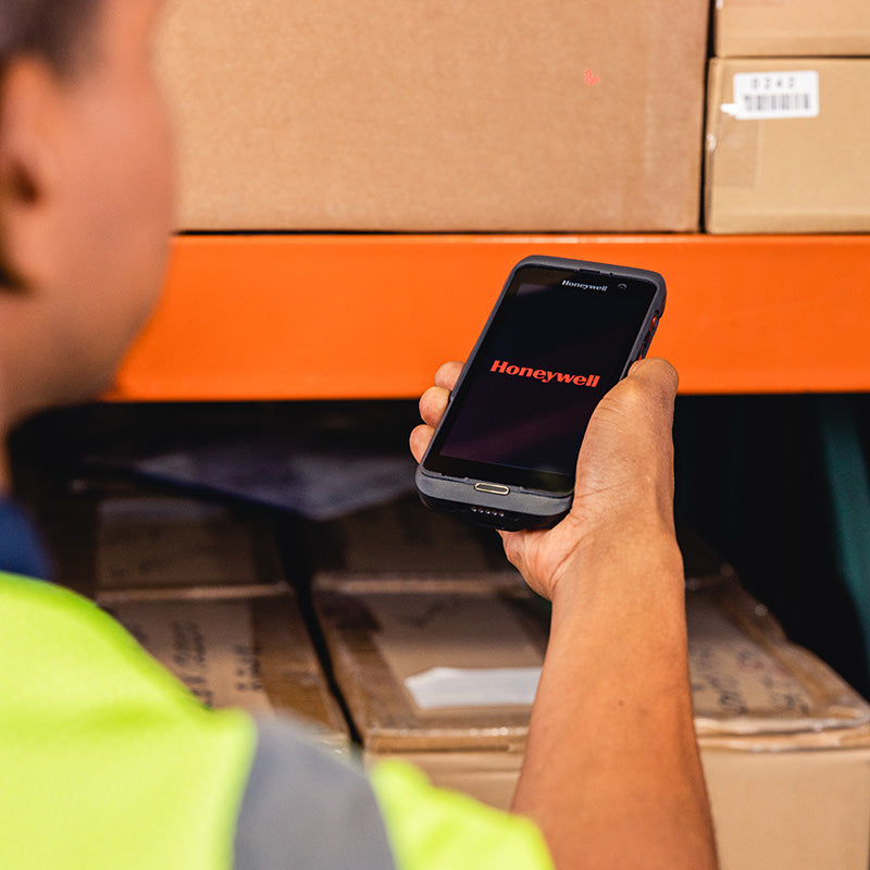 Person holding a smartphone with Honeywell logo in a warehouse setting