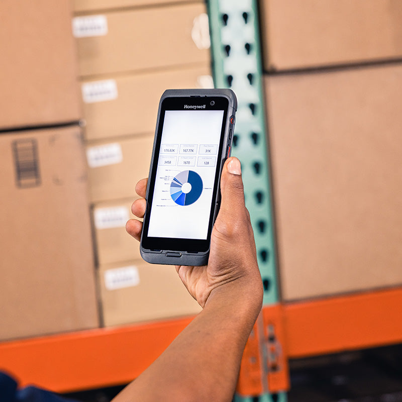 Hand holding a smartphone with a Honeywell app in a warehouse setting