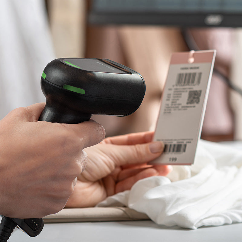 Hand using a barcode scanner to scan a product tag on a white shirt.